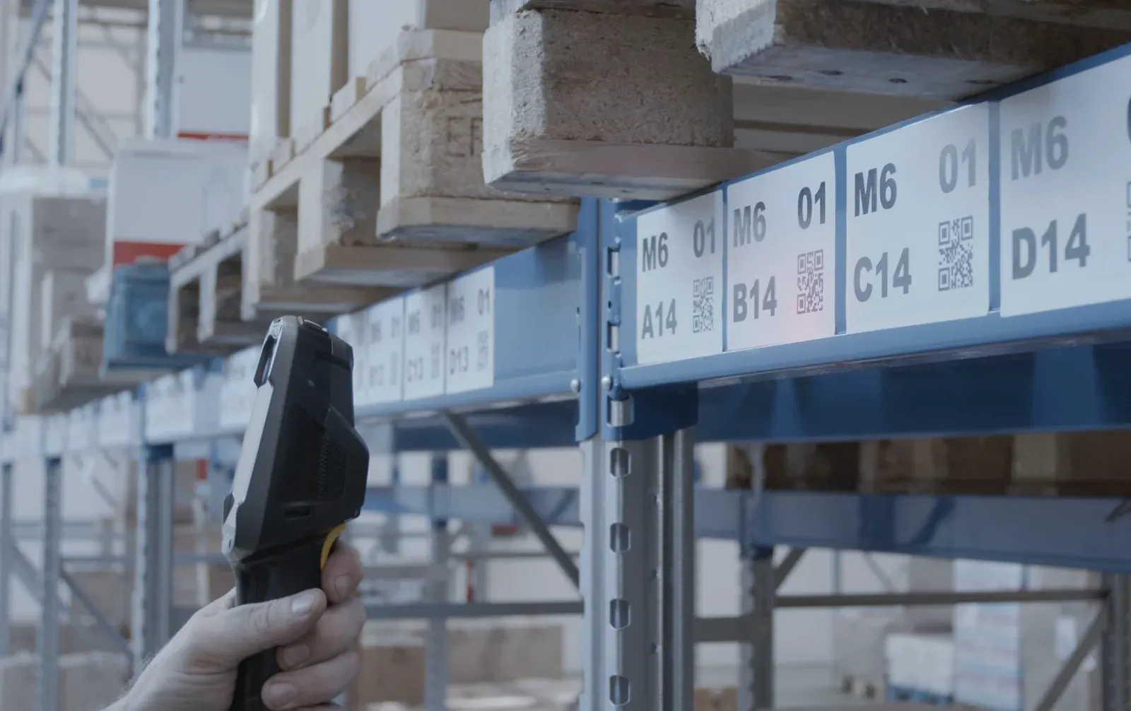 Un terminale barcode puntato verso le etichette di ubicazione di una scaffalatura di magazzino, con codici come M6 A14 e M6 B14